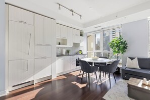 Een moderne keuken met witte kastjes, een eethoek met een tafel en stoelen, en een groot raam met uitzicht op de stad.