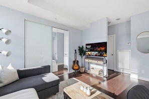 A modern living room with a grey sofa, a coffee table with decorative items, a guitar, and a television displaying a movie poster. - Stylish TO Condo CN Tower View Walk Score 99 | Parking Available (Toronto)