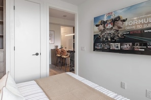 A bedroom with a bed, a wall-mounted TV displaying a Formula 1 advertisement, and a doorway leading to a kitchen area. - Yorkville Elegance 1BR Retreat | Parking Available (Toronto)