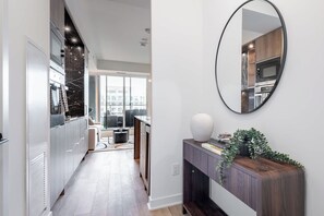 A modern kitchen with a large window, a round mirror, and a wooden console table with a vase and books. - Yorkville Elegance 1BR Retreat | Parking Available (Toronto)
