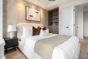 Un dormitorio moderno con una cama grande, una mesita de noche con lámpara, una obra de arte abstracta en la pared y una estantería empotrada de madera.