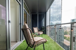 A balcony with artificial grass, two wicker chairs, and a view of a cityscape. - Luxury Yorkville 1BR Suite with Private Balcony | Parking Available (Toronto)