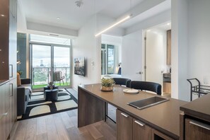 A modern kitchen with a large island, a dining area with a table and chairs, and a view of the city through large windows. - Luxury Yorkville 1BR Suite with Private Balcony | Parking Available (Toronto)