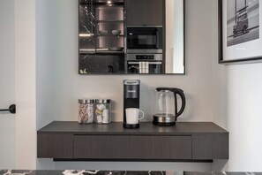 Una cocina moderna con microondas integrado, cafetera y frascos de almacenamiento sobre una encimera oscura.