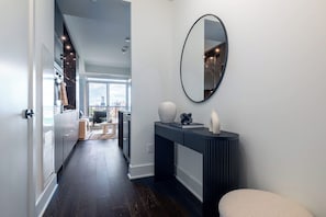 A modern hallway with a dark wood floor, a white door, and a large mirror on the wall. - Chic Yorkville 1BR Elite Living (Toronto)