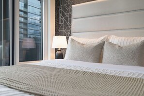 A hotel room with a large bed, a nightstand with a lamp, and a window with a view of buildings. - Chic Yorkville 1BR Elite Living (Toronto)