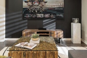 Un salon moderne avec un grand téléviseur à écran plat fixé au mur, un meuble de rangement en bois en dessous, et une table basse en verre sur laquelle sont posés un livre et une plante.