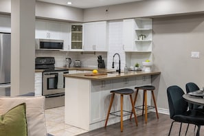 A modern kitchen with white cabinets, a central island with stools, a microwave, an oven, and a sink. - Lux 3BR Townhouse with Private Patio! | Parking Available (Toronto)