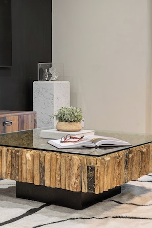 A modern living room with a glass coffee table, a wooden accent piece, a potted plant, and a pair of glasses on a book. - Lux 3BR Townhouse with Private Patio! | Parking Available (Toronto)