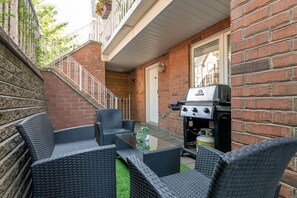 Une terrasse extérieure avec des meubles en osier, un barbecue et un mur en briques.