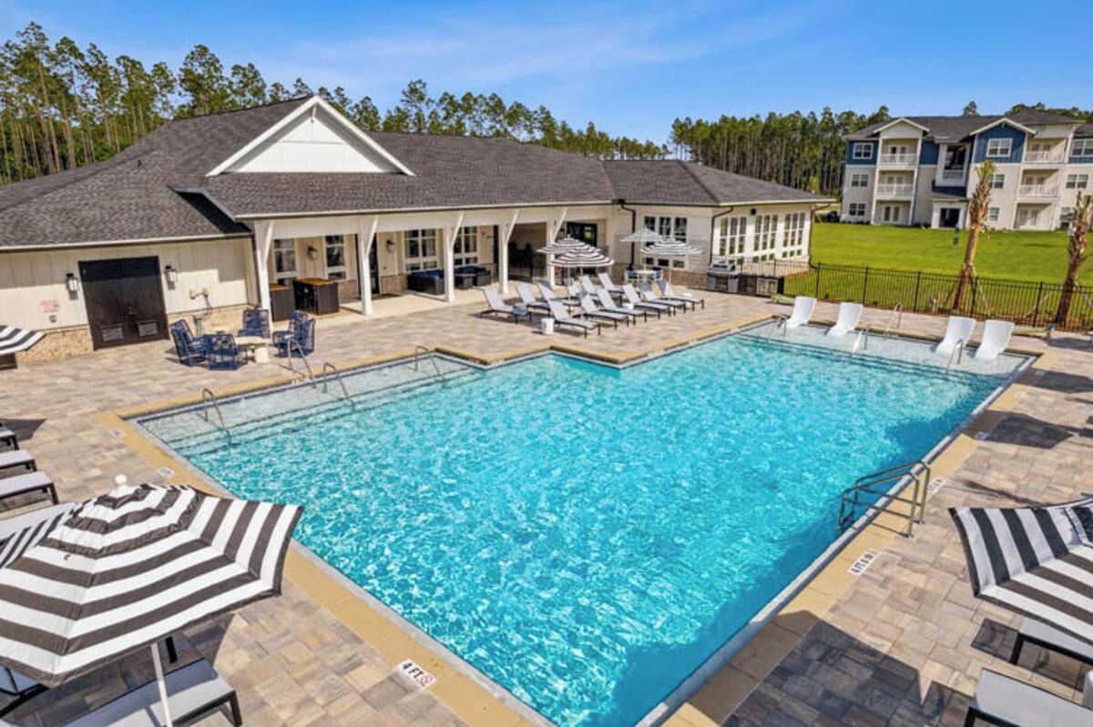 A swimming pool with lounge chairs and umbrellas, a covered patio area, and a building with a gabled roof.