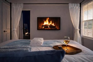 A bedroom with a fireplace, a bed with a blue blanket, a glass of wine, and a tray. - Wildlight Retreat · Pool · Pickleball · Canopy Bed (Yulee)