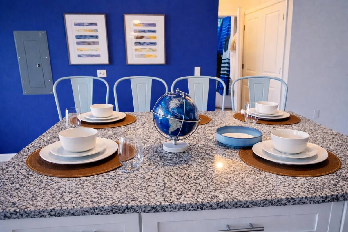A dining area with a granite countertop, white chairs, a globe centerpiece, and framed artwork on the wall.