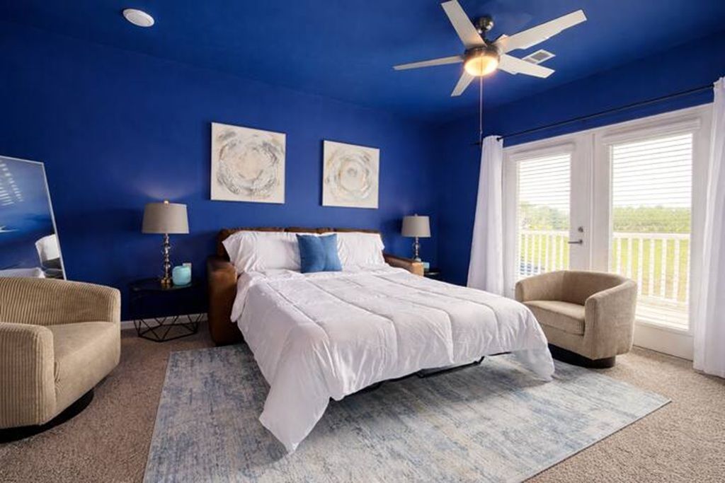 A bedroom with a bed, two side tables, a ceiling fan, and a view through a window.