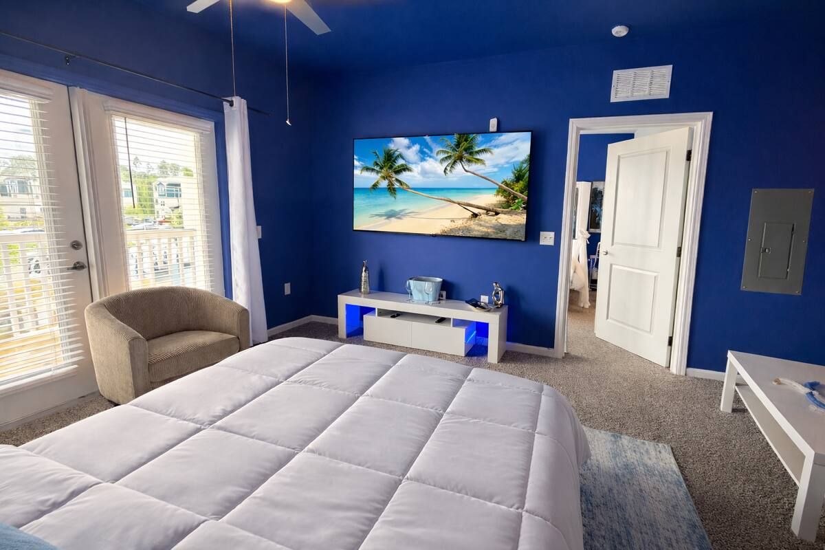 Ein Schlafzimmer mit einem großen Bett, einem Wandfernseher, einem Sessel und einer Tür zu einem weiteren Raum.