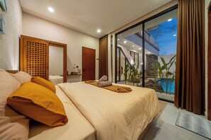 A hotel room with a bed, a wooden door, a bathroom, and a view of a swimming pool. - Green Roof Villa Pandawa (KAB. BADUNG)