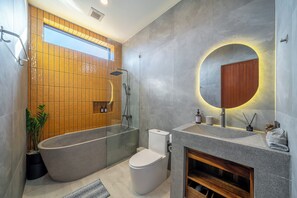 A modern bathroom with a freestanding bathtub, a toilet, a vanity with a mirror, and a shower area. - Green Roof Villa Pandawa (KAB. BADUNG)