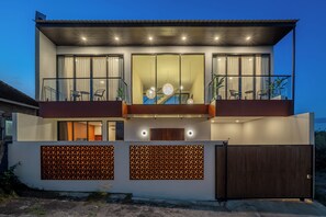 A modern two-story building with a balcony, large windows, and a wooden door. - Green Roof Villa Pandawa (KAB. BADUNG)
