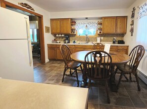 A kitchen with wooden cabinets, a dining table with chairs, a refrigerator, and a window with a curtain. - Starlight Retreat located near Pictured Rocks and access to ATV/Snowmobile Trail (Shingleton)