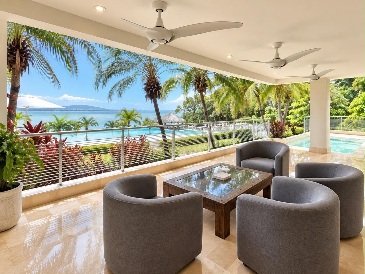 A balcony with a view of a pool and palm trees, furnished with grey chairs and a glass-top table.