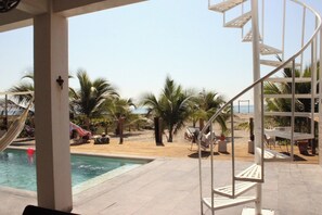 A pool area with a spiral staircase, palm trees, and a beach view. - Casa Macali · Planta Alta · Frente al Mar · 2 Recámaras + Estudio · Hasta 6 (Campamento Cerro Hermoso)
