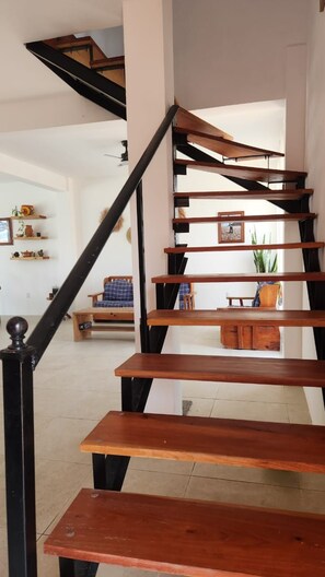 A wooden staircase with black railings leading to an upper floor. - Casa Macali · Planta Alta · Frente al Mar · 2 Recámaras + Estudio · Hasta 6 (Campamento Cerro Hermoso)