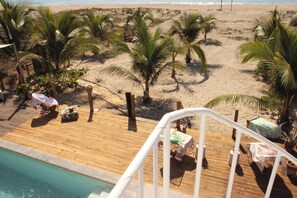 Um deck de madeira com piscina, palmeiras e vista para a praia.