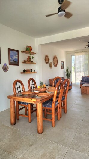 Uma sala de jantar com uma mesa e cadeiras de madeira, um ventilador de teto e prateleiras decorativas na parede.