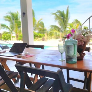 A wooden table with a laptop, a glass, and a vase with flowers. - Casa Macali · Planta Alta · Frente al Mar · 2 Recámaras + Estudio · Hasta 6 (Campamento Cerro Hermoso)
