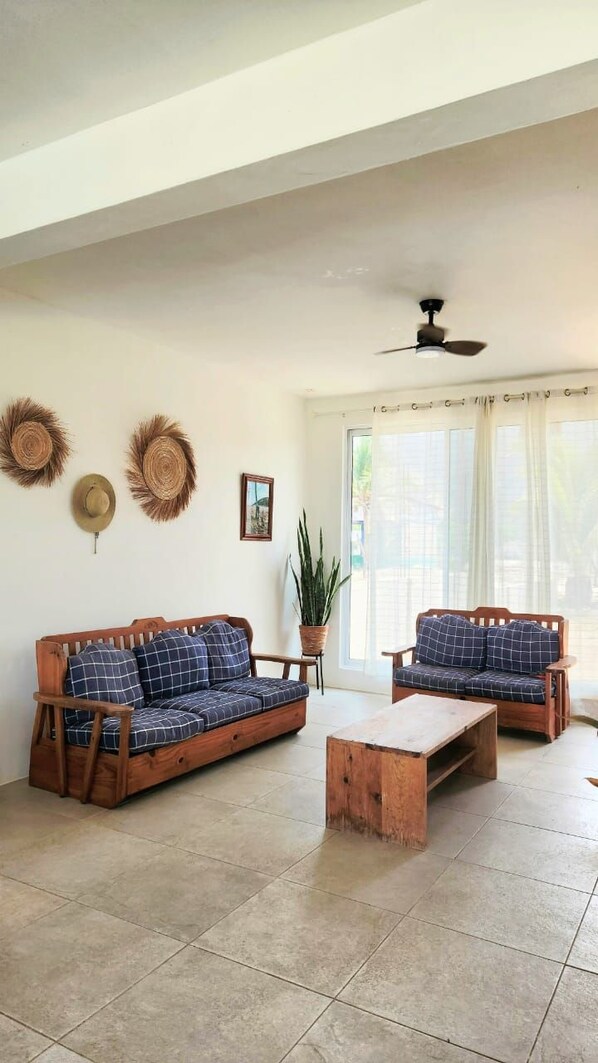A room with two wooden sofas with checkered cushions, a wooden coffee table, and a ceiling fan.
