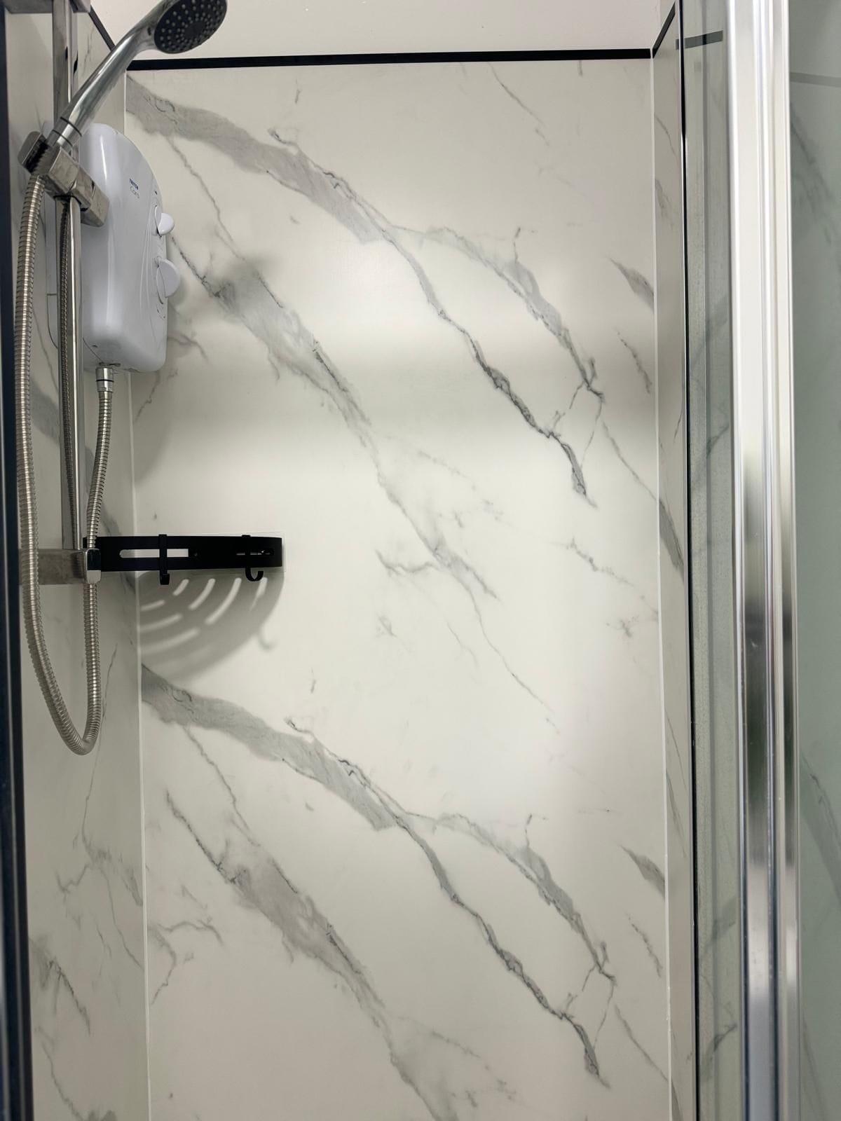 A shower enclosure with a marble-patterned wall and a handheld showerhead.