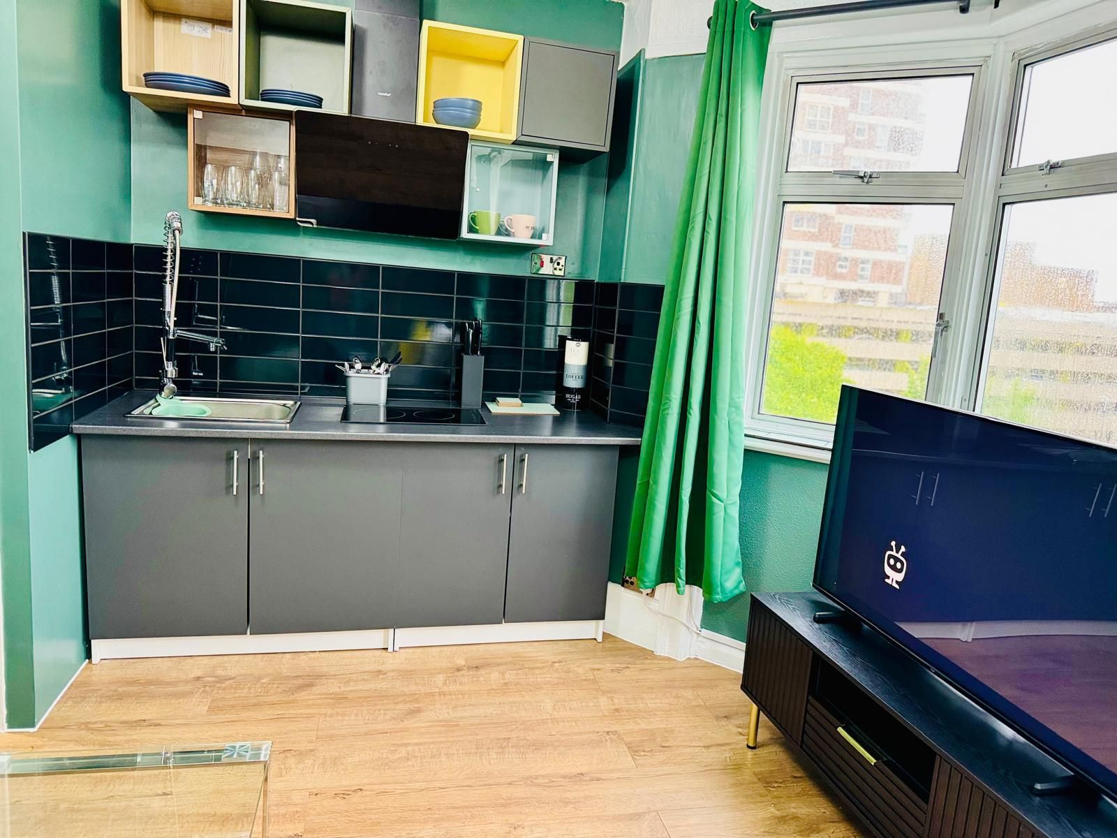 A modern kitchen with grey cabinets, a black countertop, and a window with green curtains.