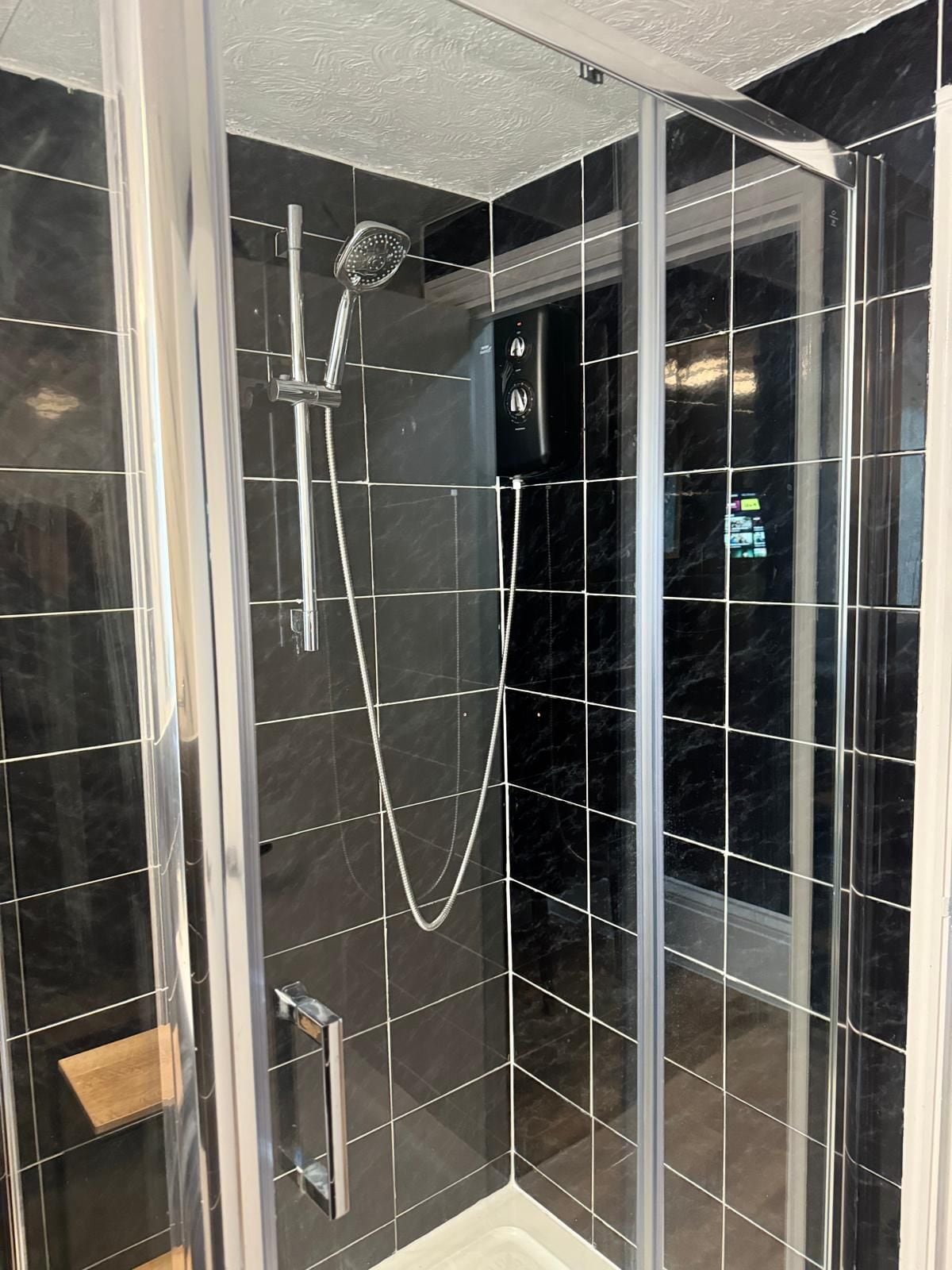 A glass-enclosed shower with a handheld showerhead and a wall-mounted control panel.
