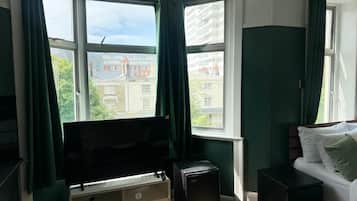 Una habitación con un ventanal grande, una cama, un televisor y un electrodoméstico pequeño.