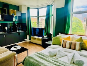 Habitación de hotel moderna con cama, televisor, kitchenette y vistas de la ciudad.