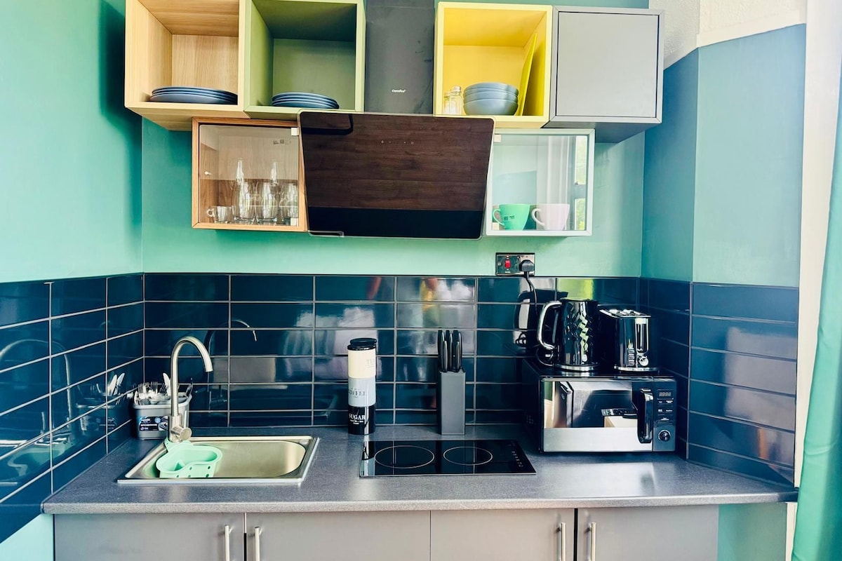 Una cocina con pileta, estufa y microondas. Hay repisas sobre la encimera con vajilla y vasos.