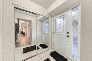 A hallway with a sliding glass door, a white door with a decorative glass panel, and a black doormat. - Spacious Toronto nest 6BR/4.5BA, Free Parking, 2 kitchens near 401 & Zoo (Toronto)