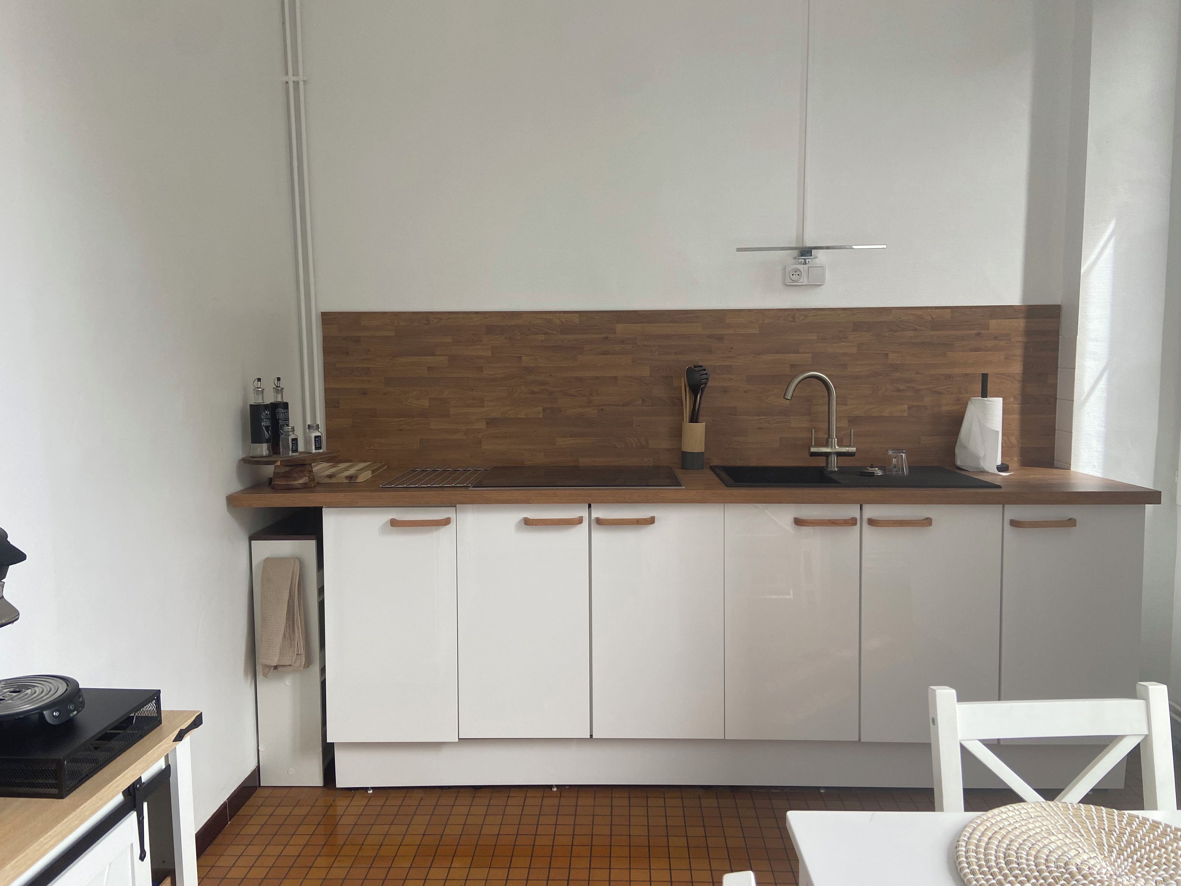 Een compacte keuken met een houten spatwand, witte kasten, een zwart aanrecht en een enkele gootsteen.