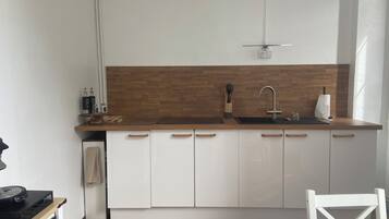 Een compacte keuken met een houten spatwand, witte kasten, een zwart aanrecht en een enkele gootsteen.