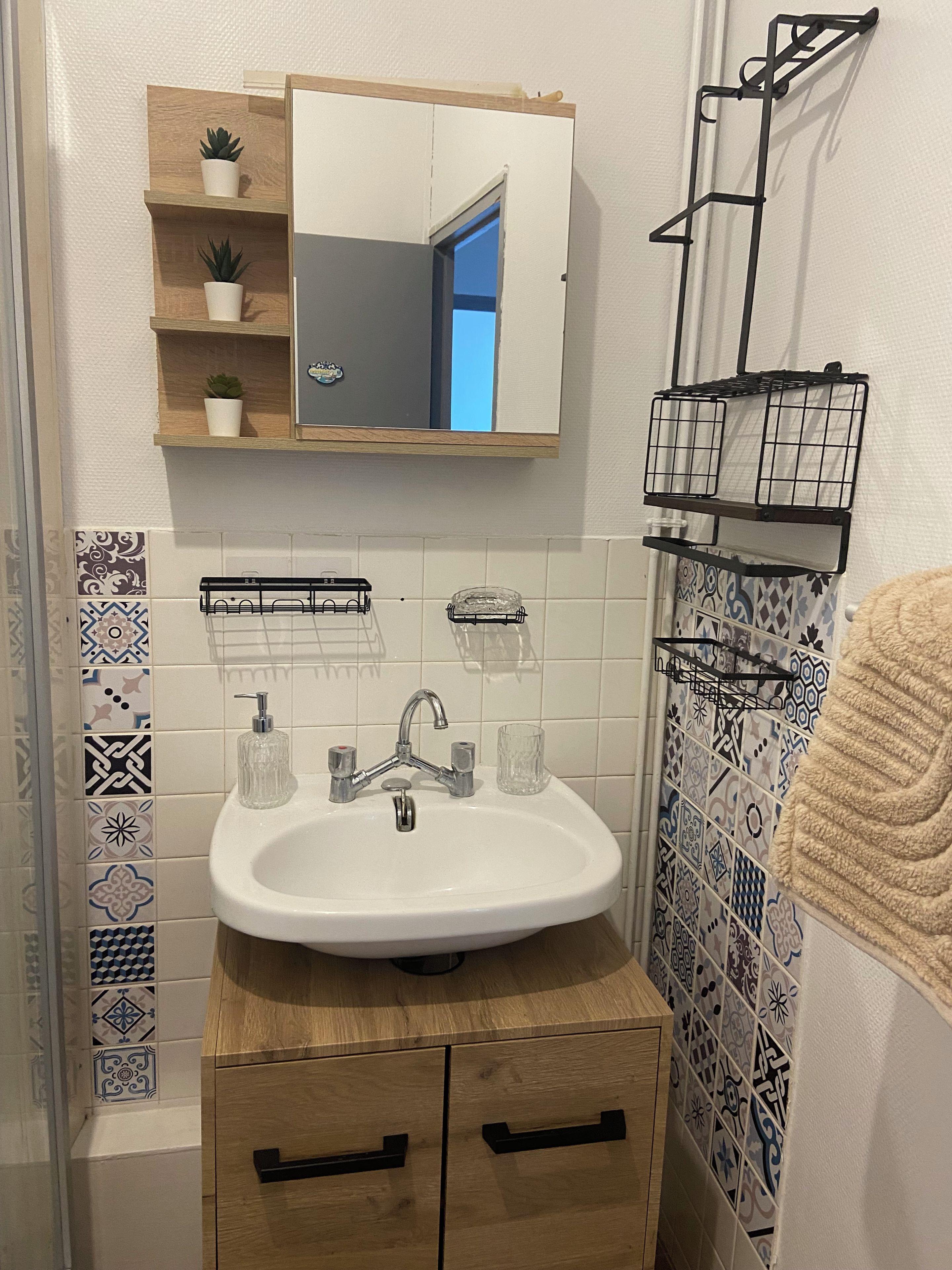 Een badkamer met een witte wastafel, een spiegel erboven, een houten kastje eronder en een handdoekhouder aan de rechterkant.
