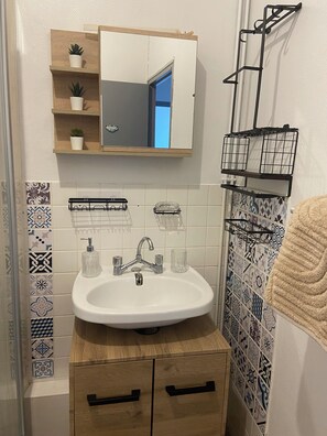 Een badkamer met een witte wastafel, een spiegel erboven, een houten kastje eronder en een handdoekhouder aan de rechterkant.