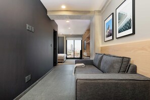 A modern hotel room with a grey sofa, a bed, and a city view through large windows. - w* | Enchanting Loft w/ Balcony in Tabacalera (Ciudad de México)