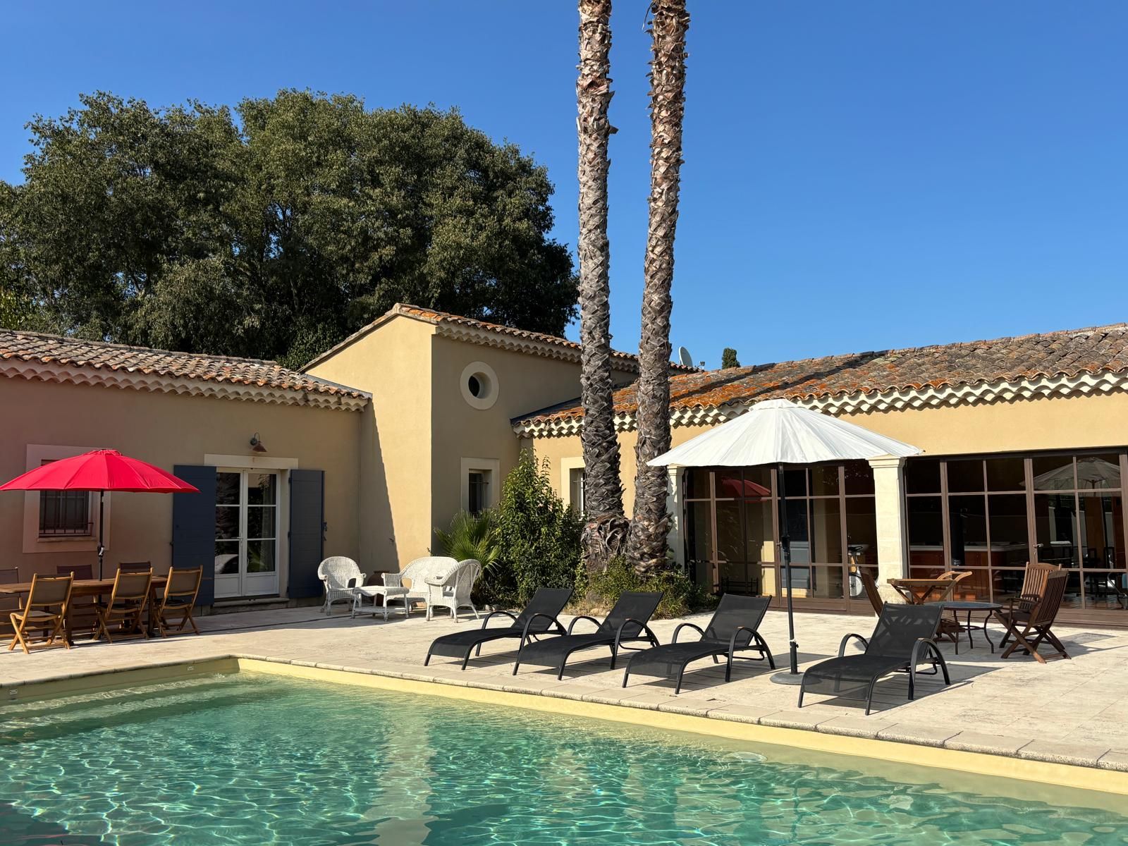 A pool area with lounge chairs and umbrellas, surrounded by buildings with tiled roofs.