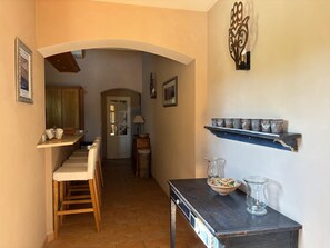 A kitchen with a wooden table, chairs, and a shelf with cups. - A Magnificent Haven of Peace (Mas-Blanc-des-Alpilles)
