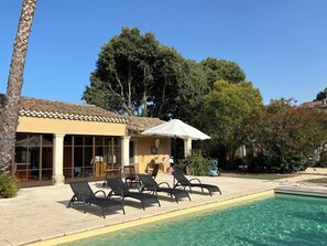 A poolside area with lounge chairs, a covered seating area, and a building with large windows. - A Magnificent Haven of Peace (Mas-Blanc-des-Alpilles)