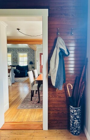 An interior space with a wooden floor, a dining area with chairs and a table, a hallway with a coat rack, and a patterned vase on the floor. - Charming Newly Renovated Downtown Winter Harbor Retreat - Minutes to Schoodic! (Winter Harbor)