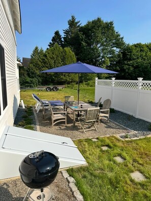Un patio con una parrilla, mobiliario exterior y una valla blanca.