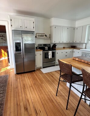 A modern kitchen with stainless steel appliances, white cabinetry, and a wooden floor. - Charming Newly Renovated Downtown Winter Harbor Retreat - Minutes to Schoodic! (Winter Harbor)
