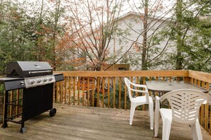 A deck with a grill, two white plastic chairs, and a table. - Stunning Poconos Mountain Retreat with Spacious Rooms, Pool Table and Family Fun (Tobyhanna)