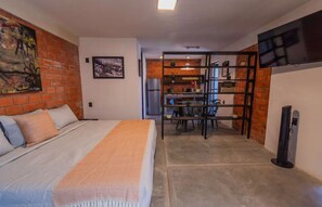 A bedroom with a bed, a dining area with chairs and a table, and a kitchen area with a refrigerator and shelves. - Loft with a King-size bed in San Felipe (Oaxaca de Juárez)